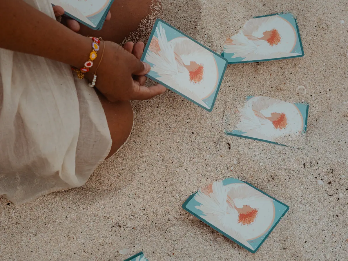 Manos de Blanca extendiendo las cartas del Oráculo Angelical sobre la arena, en un círculo de guía y autoconocimiento
